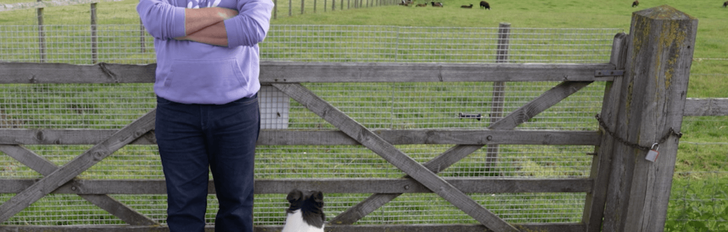 Photo of Rob Nicholson and a sheepdog in front of a farm gate