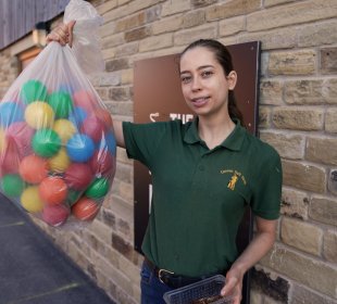 Photo of Kate holding a sack of plastic multi coloured toy balls which will create a ball-pit for the meerkats